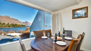 A dining area with a table set for two, a view of a lake and mountains, and a painting on the wall.