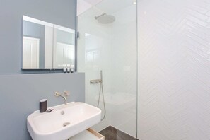 A modern bathroom with a glass-enclosed shower, a white sink, and a mirror above it.