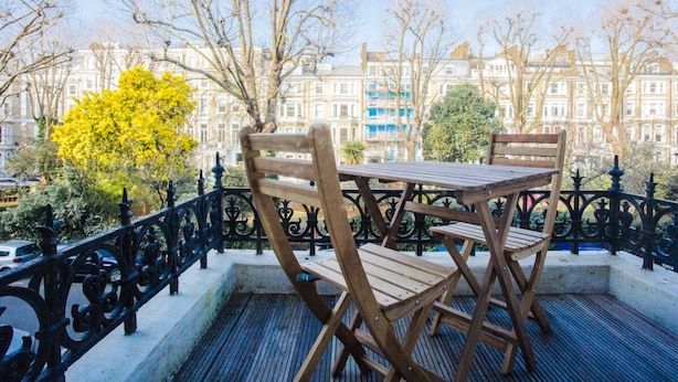 A wooden table and chairs on a balcony with a wrought iron railing, overlooking a row of buildings. - Modern & Spacious 1 Bedroom Apartment in London (London)