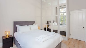 A neatly made bed with white linens and towels, a grey upholstered headboard, and a bedside table with a lamp. - Modern & Spacious 1 Bedroom Apartment in London (London)