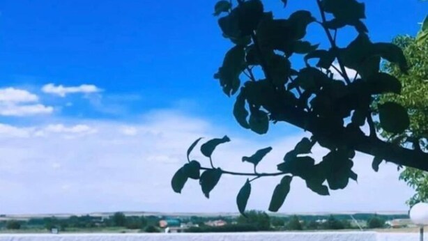Piscina retangular com cerca de madeira em primeiro plano, céu azul límpido e vista para um corpo de água ao fundo.