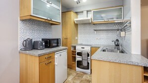 Eine kompakte Küche mit Holdekor-Schränken, einer Mikrowelle, einem Wasserkocher, einem Toaster, einem kleinen Kühlschrank und einem Backofen.