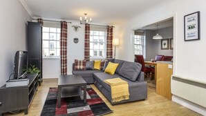Ein modernes Wohnzimmer mit einem grauen Ecksofa, einem Flachbildfernseher und einem Essbereich mit Holztisch und Stühlen.