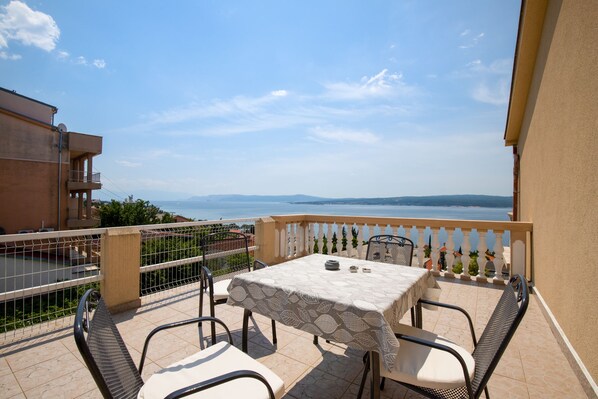 A balcony with a table and chairs, overlooking a body of water and distant mountains.