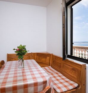 A room with a checkered table and bench, a potted plant, and a window with a view of the sea.