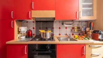 A modern kitchen with red cabinets, a coffee maker, a stove, and various kitchen utensils.
