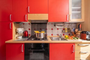 A modern kitchen with red cabinets, a coffee maker, a stove, and various kitchen utensils.