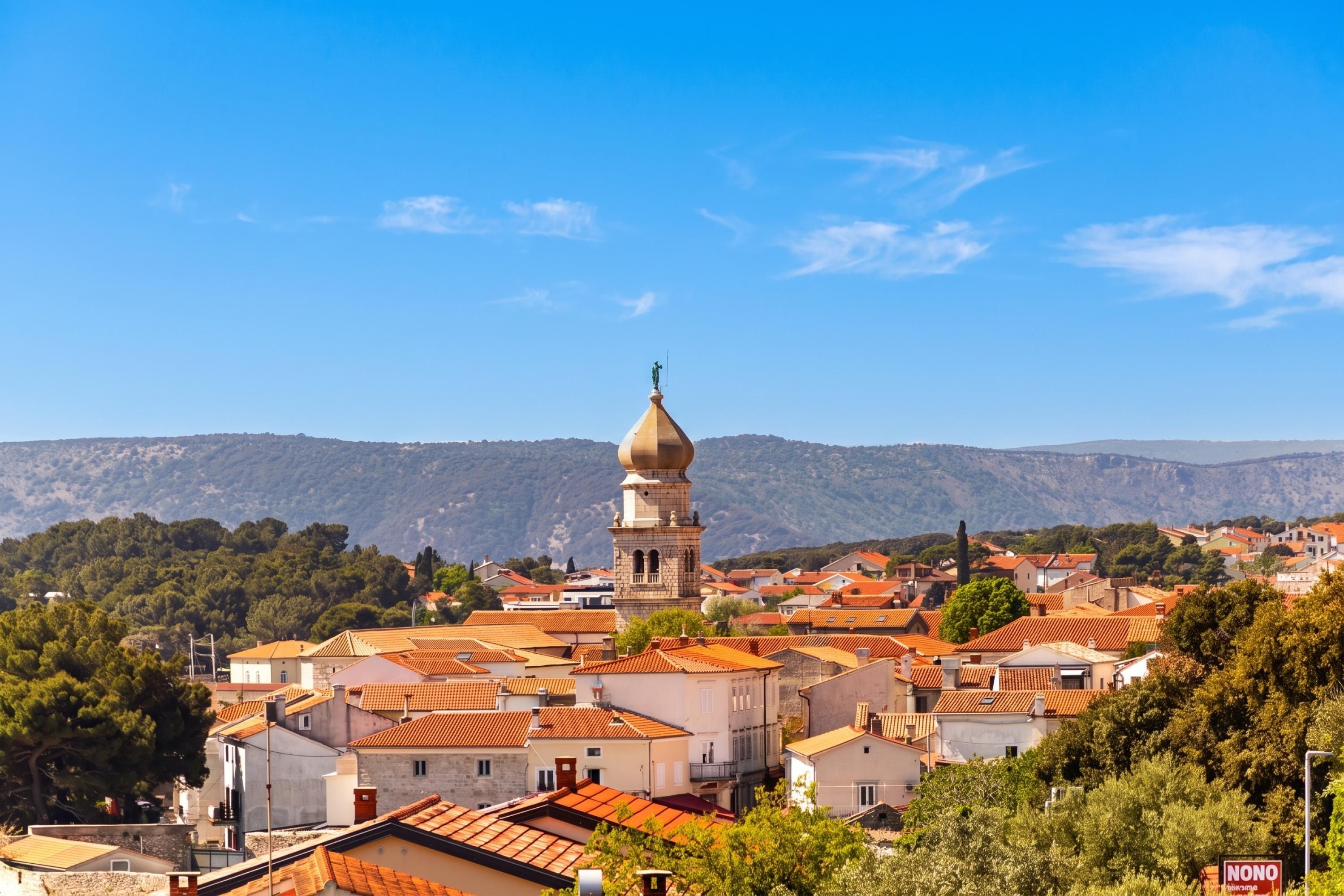 Une ville où se dresse une église remarquable, dotée d’un dôme et d’un clocher, entourée de bâtiments aux toits recouverts de tuiles rouges, le tout sur fond de montagnes.