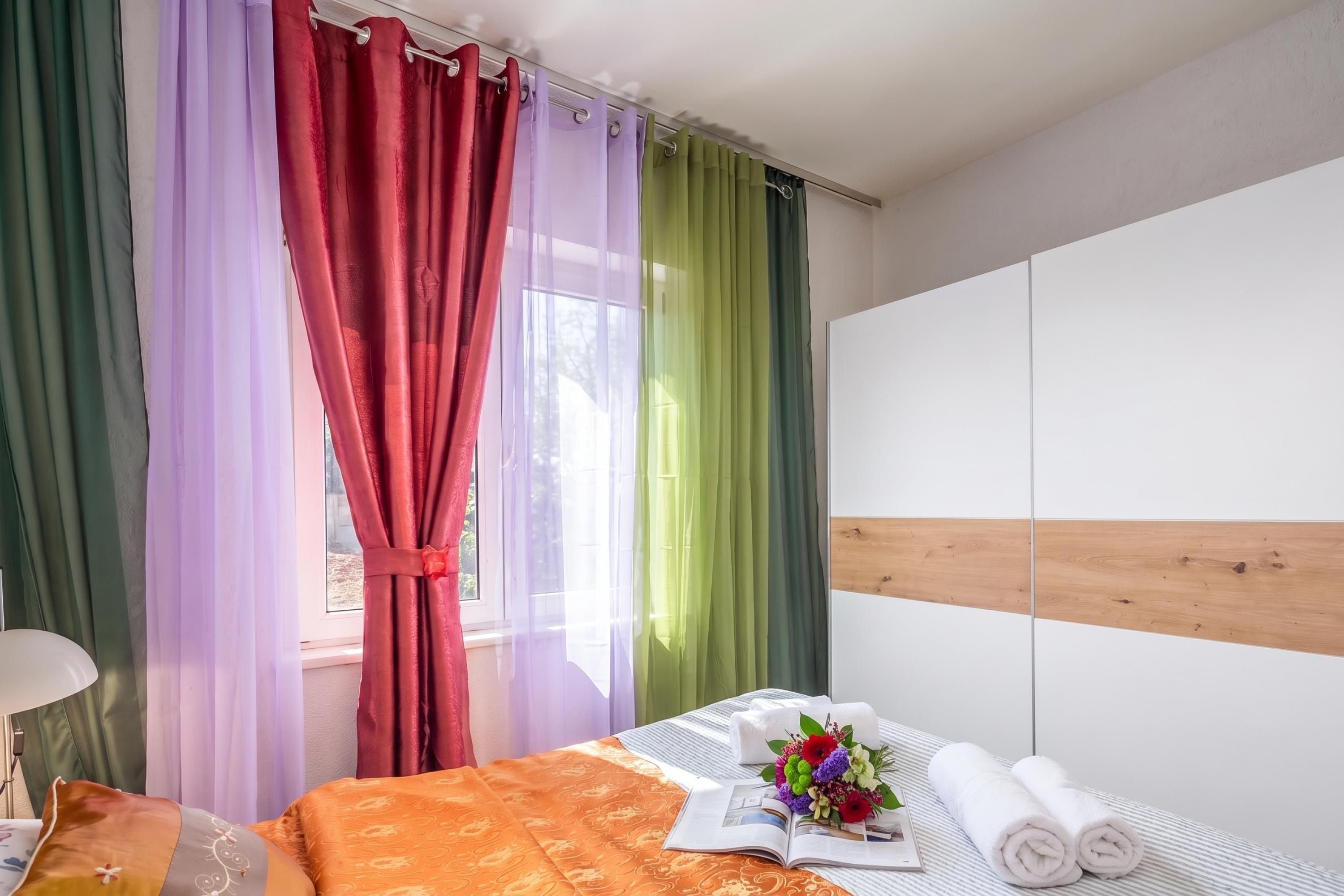 A hotel room with a bed, a bedside table with a book and flowers, and a wardrobe.