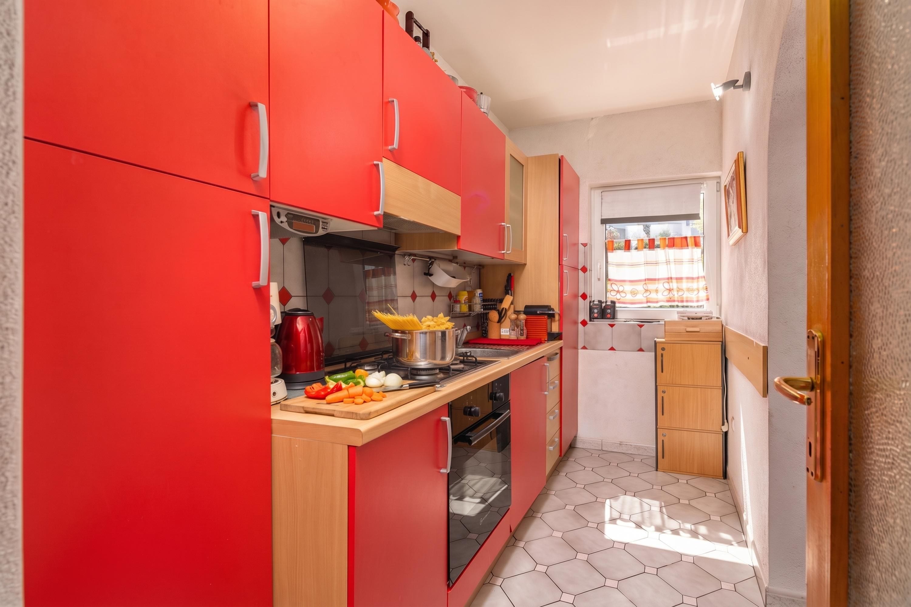 Uma cozinha compacta com armários vermelhos, bancada de madeira e janela com cortinas.