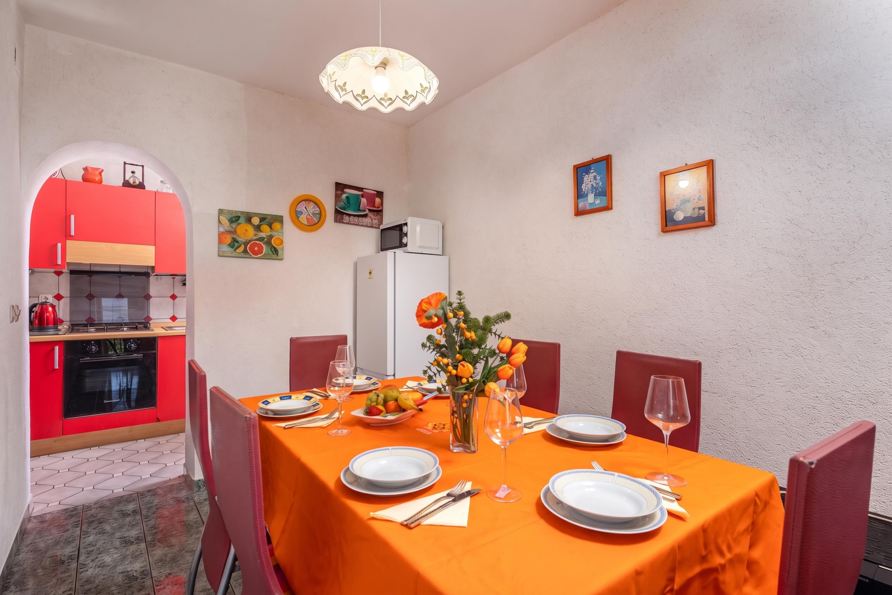 A dining area with a table set for two, a kitchen in the background, and decorative wall art.