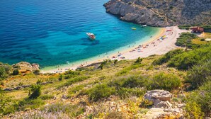 Una spiaggia costiera con acque blu cristalline, terreno roccioso e alcune imbarcazioni.