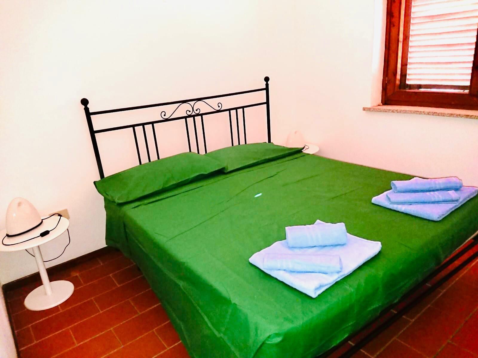 A single bed with a green bedspread and two folded towels on it.