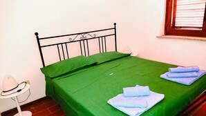 A single bed with a green bedspread and two folded towels on it. - Quadrilocale Gallura (San Teodoro)