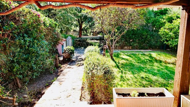 A garden pathway leading to a wooden structure with a white planter box on a table. - Quadrilocale Gallura (San Teodoro)