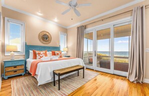 A bedroom with a bed, a bench, a nightstand, a lamp, a ceiling fan, and a view of the ocean through a sliding glass door. - CJ's Beach Front 6 BR Heated Pool Private Home (St. George Island)