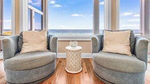 A seating area with two grey armchairs and a small white side table, positioned in front of large windows with a view of the ocean. - CJ's Beach Front 6 BR Heated Pool Private Home (St. George Island)