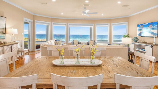 A spacious living room with a large wooden dining table, multiple seating options, and a view of the ocean through large windows. - CJ's Beach Front 6 BR Heated Pool Private Home (St. George Island)