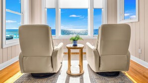 A room with two beige armchairs facing a large window overlooking the ocean. A small wooden table with a potted plant is in the center. - CJ's Beach Front 6 BR Heated Pool Private Home (St. George Island)