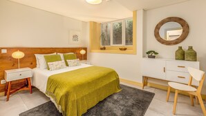 Un dormitorio con cama, mesitas de noche, cómoda, silla, ventana y espejo.