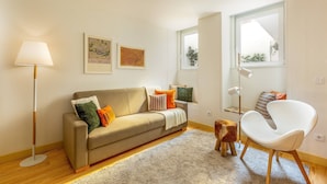 Una sala moderna con un sofá, una silla, una lámpara de pie y un taburete de madera.
