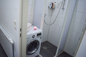 Une petite buanderie comprenant un lave-linge, des toilettes et un espace douche.