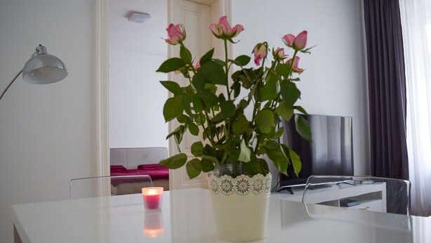 A white table with a vase of pink roses, a lit candle, and a modern lamp. - Modern apartment in Vienna near Danube (Vienna)