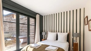 A hotel room with a bed, a nightstand, a lamp, a window with curtains, and a view of the outside. - La Terrasse de Pom | Cozy Comfort | City Center | 2 Guests (Honfleur)