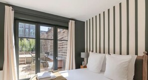 Ein Hotelzimmer mit Bett, Nachttisch, Lampe und Blick ins Freie.