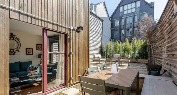 A wooden exterior with a sliding glass door leading to a living area with a sofa and a coffee table.