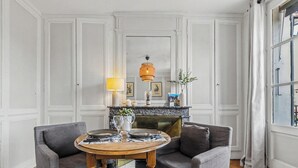 Une pièce avec une cheminée, une table ronde entourée de chaises et une fenêtre avec des rideaux.