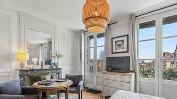 Een hotelkamer met een eettafel, een bank, een televisie en een groot raam met uitzicht op een stadsbeeld.