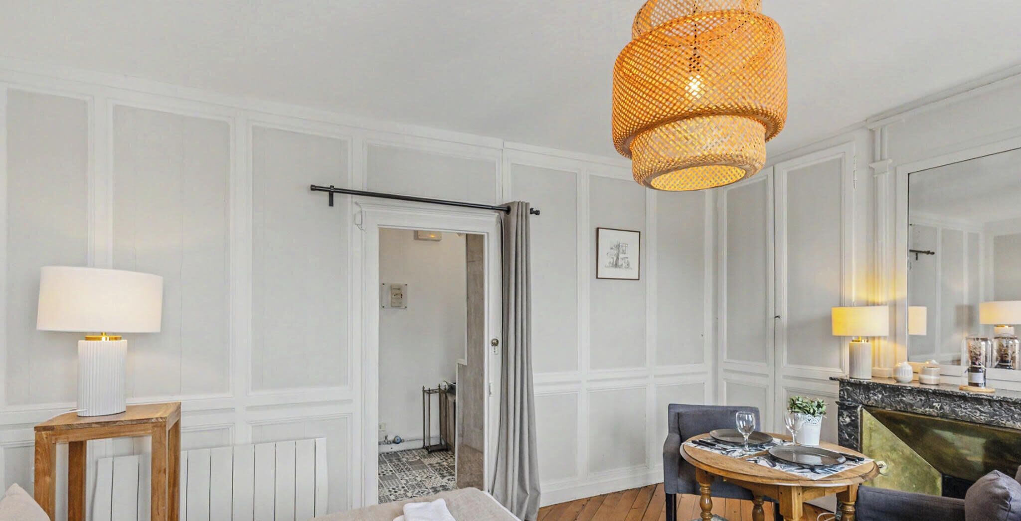 A hotel room with a dining area, a fireplace, a large mirror, and a hanging light fixture.
