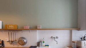 Una cocina con baldosas blancas, un estante de madera con utensilios de cocina, un tostador y un hervidor.