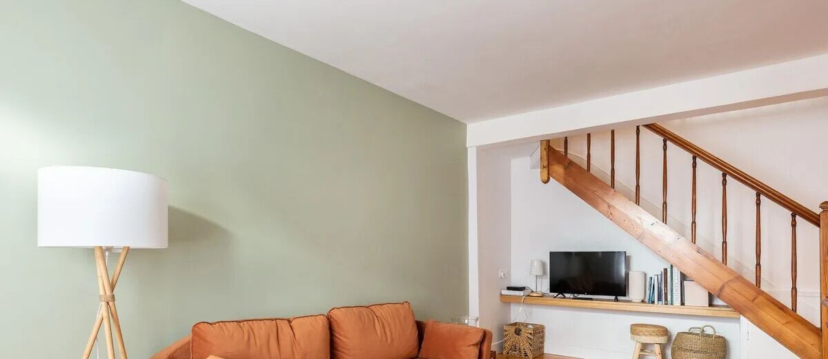 A living room with a sofa, a lamp, a television, and a wooden staircase.