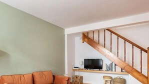 Una sala de estar con un sofá, una lámpara, un televisor y una escalera de madera.