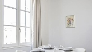 Un comedor con una mesa dispuesta para cuatro, una ventana con cortinas y un cuadro floral en la pared.