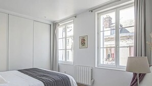Un dormitorio con cama, mesita de noche, ventana y radiador.