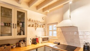 A kitchen with a microwave, kettle, and a gas stove. There are cabinets with glass doors and shelves above the counter. - La Belle Place | City Center | 4 Guests (Honfleur)