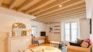 A cozy living room with a dining area, wooden beams on the ceiling, a fireplace, and a television. - La Belle Place | City Center | 4 Guests (Honfleur)