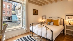 A bedroom with a bed, a window, a chair, and a nightstand. - La Belle Place | City Center | 4 Guests (Honfleur)