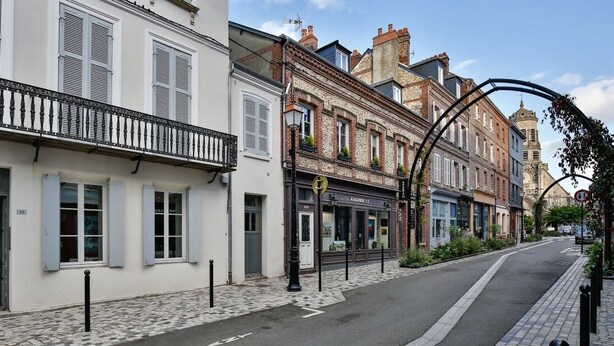 Rua com edifícios, calçada de paralelepípedos e céu limpo.