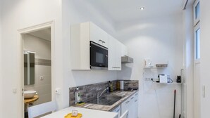 Cozinha compacta com armários brancos, micro-ondas embutido, pia e bancada com chaleira.