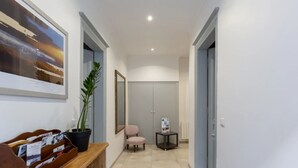 Um corredor com um quadro emoldurado, uma planta em vaso, uma cadeira, uma mesinha e um guarda-roupa.