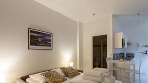 Quarto de hotel moderno com cama, pintura, cozinha compacta e banheiro visível por uma porta aberta.