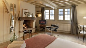 A cozy room with a fireplace, a bed, a TV, and a window with curtains. - Couleur Corail Studio – Peaceful gem & shared yard – Central Honfleur (Honfleur)