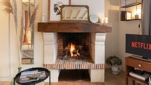 A living room with a fireplace, a bookshelf, and a television. - Couleur Corail Studio – Peaceful gem & shared yard – Central Honfleur (Honfleur)