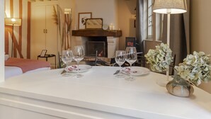A hotel room with a dining table set for two, a vase with flowers, and a fireplace in the background. - Couleur Corail Studio – Peaceful gem & shared yard – Central Honfleur (Honfleur)