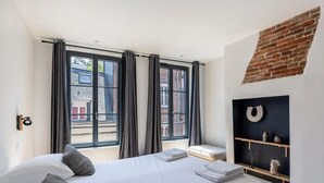 Une chambre moderne avec un lit, un banc, une étagère fixée au mur et de grandes fenêtres.