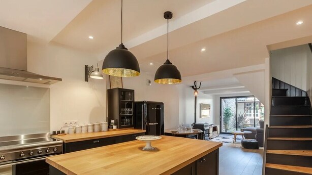 Une cuisine moderne avec un îlot central en bois, des suspensions noires et une cuisinière en acier inoxydable.